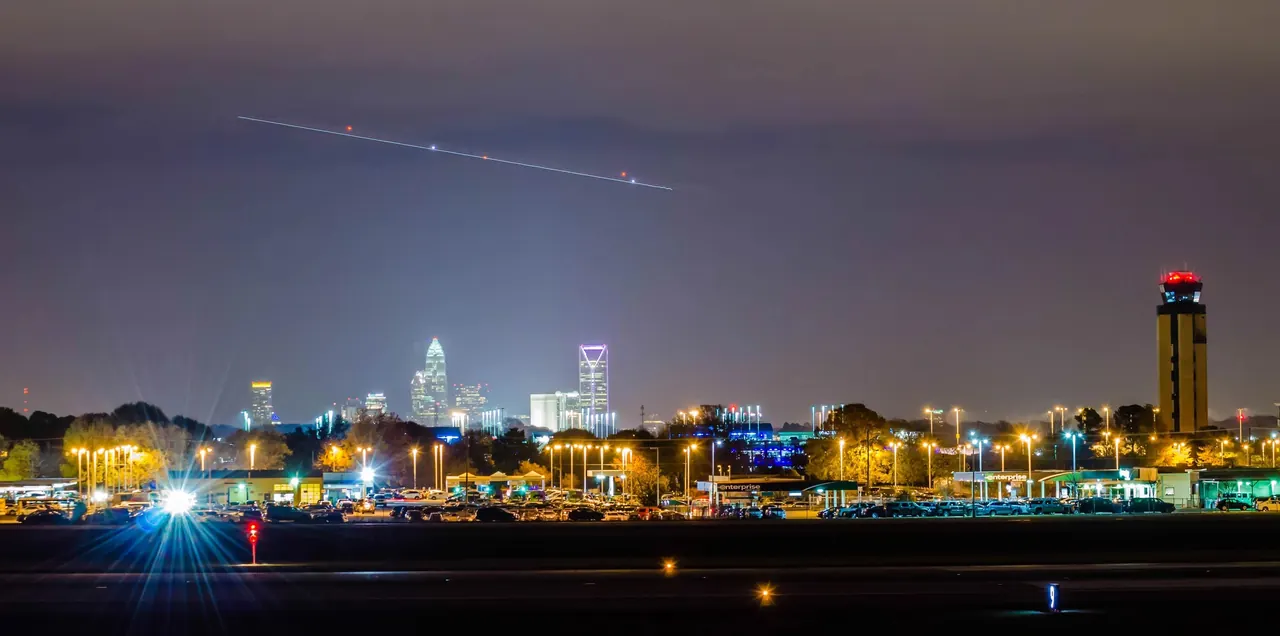 The Charlotte Douglas control tower and the Charlotte skyline at night, with the light trail of an aircraft overhead