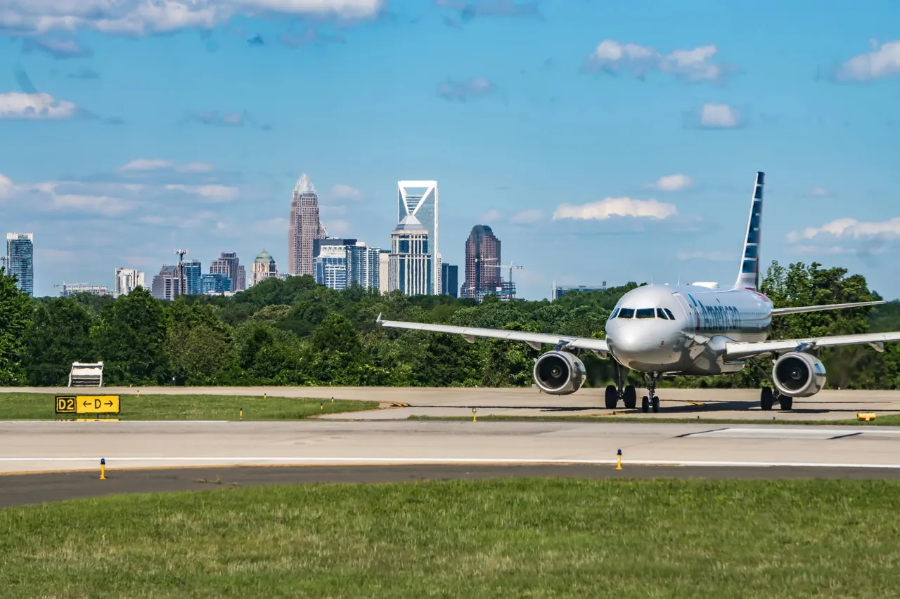 An American Airlines jet taxiing at Charlotte Douglas International Airport with the Charlotte skyline behind the trees