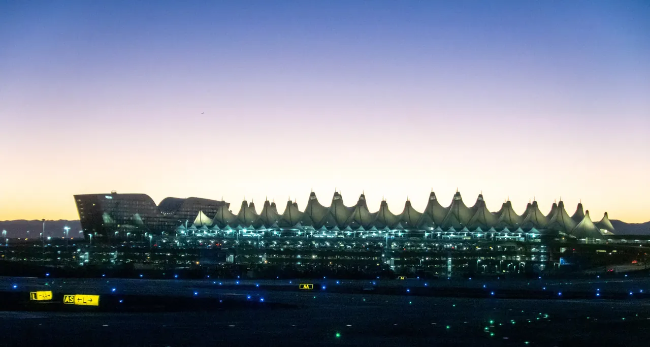 The white tent-roof terminal at Denver International Airport lit against a dusk sky, seen across the airfield