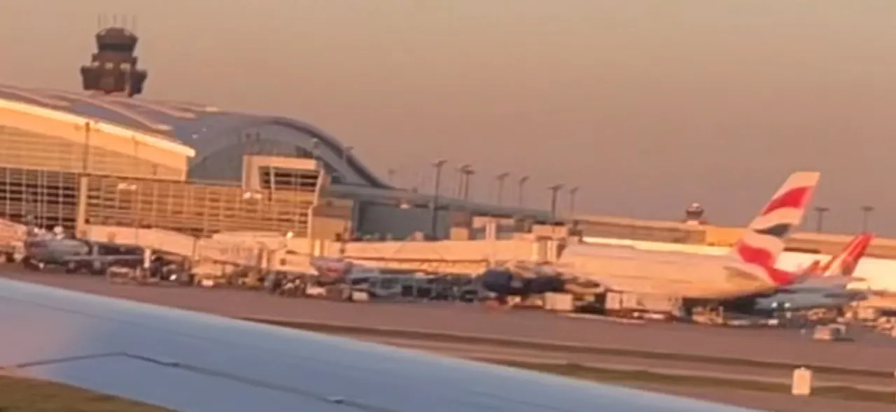 Terminal and control tower at Dallas Fort Worth International Airport seen past an aircraft wing, with a British Airways jet at the gate