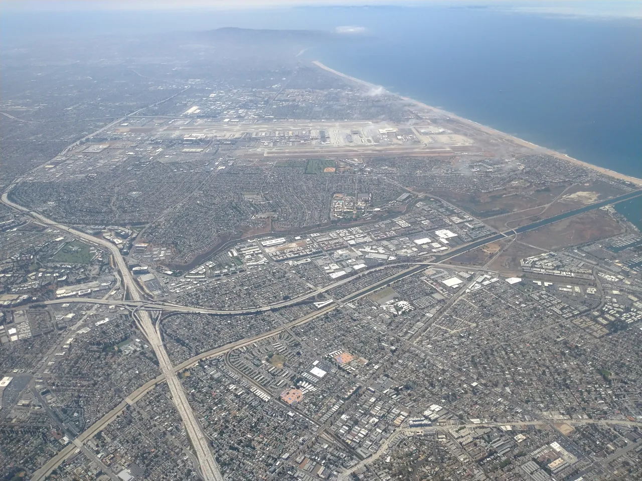 Aerial view of Los Angeles International Airport beside the Pacific coast, with freeways and neighborhoods in the foreground and haze over the ocean