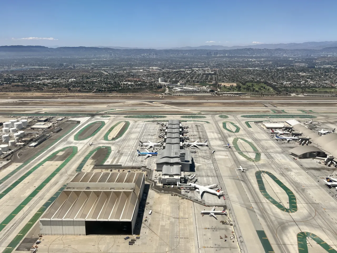Aerial view of Los Angeles International Airport, with terminal buildings, aircraft at the gates and parallel runways, and hills and city beyond