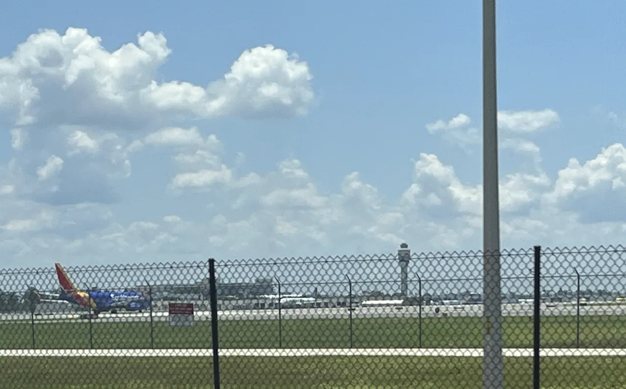 A Southwest Airlines jet and the Orlando International Airport control tower seen across the airfield fence