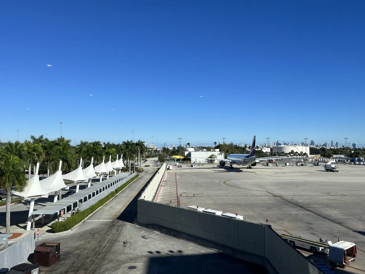 The white tent-style canopies along a concourse and the apron at Miami International Airport under a clear blue sky