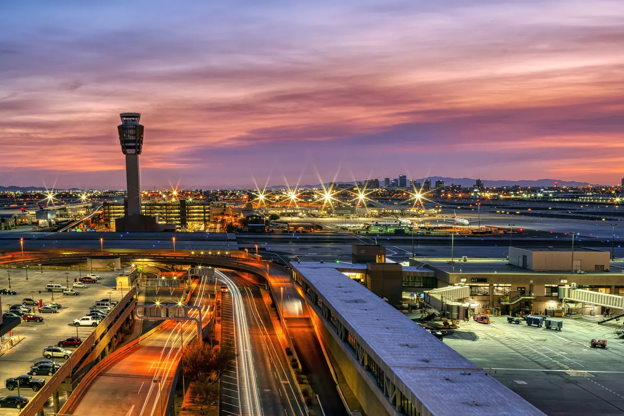 The Phoenix Sky Harbor control tower and terminal roadways at sunset, with the downtown Phoenix skyline in the distance