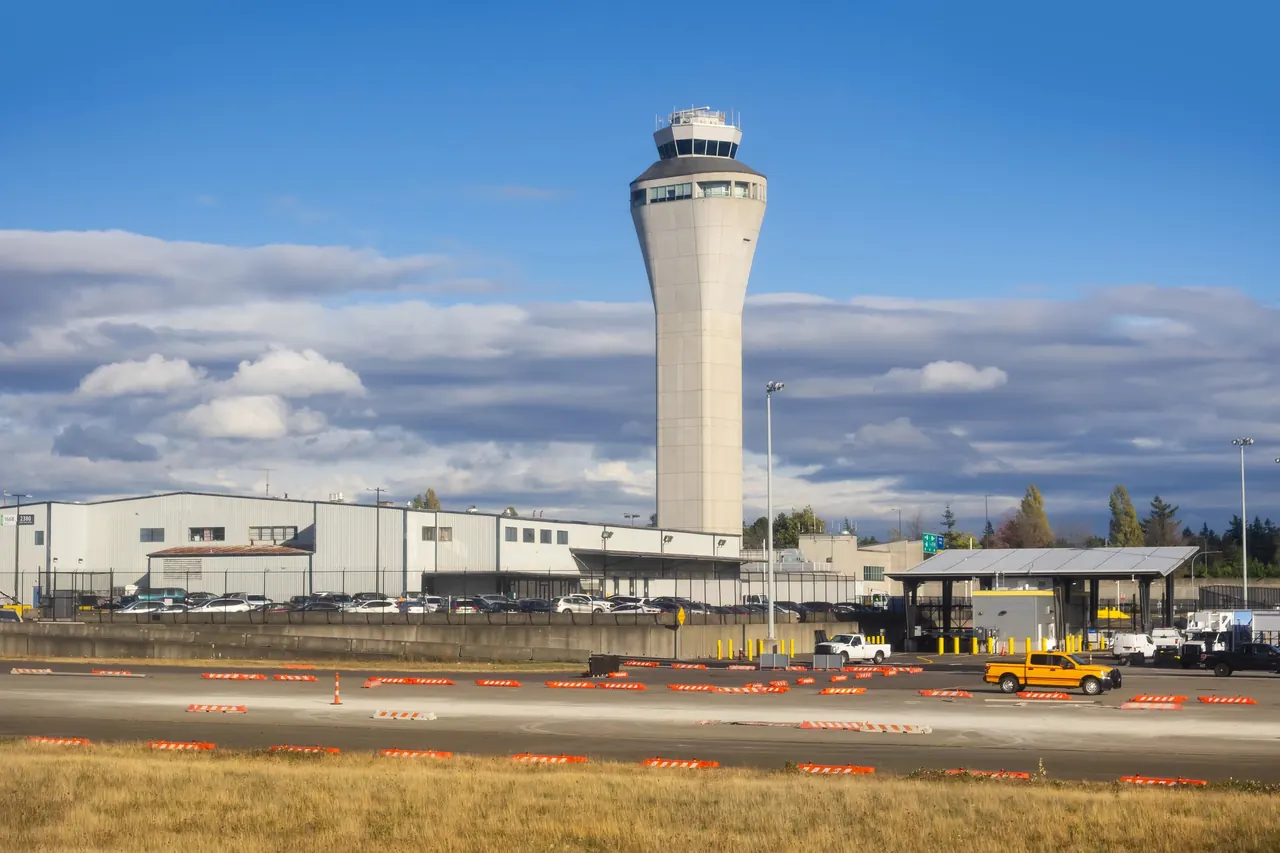 The Seattle-Tacoma International Airport control tower rising above airport buildings under a blue sky with broken cloud