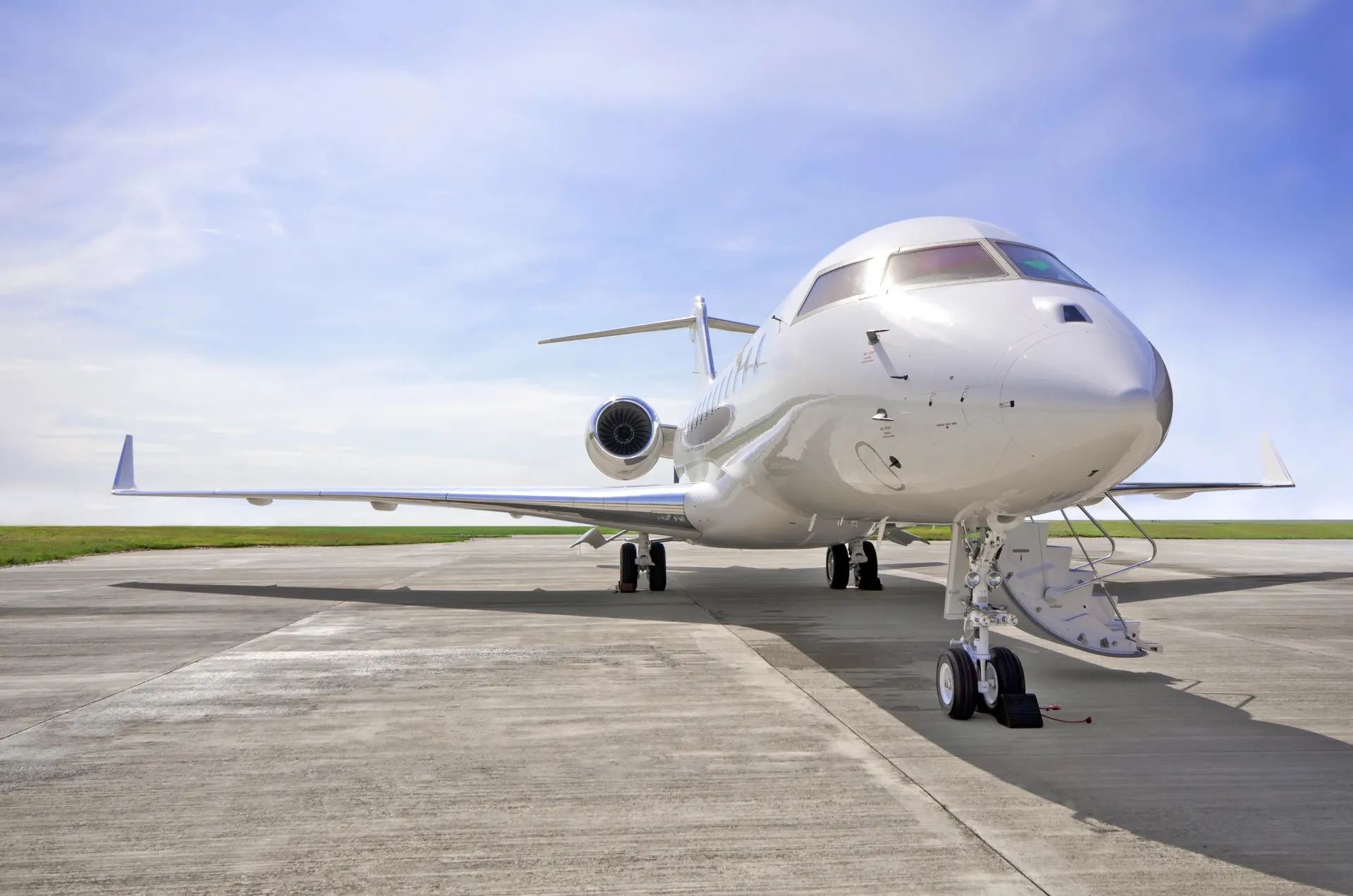 A white Bombardier Global business jet parked on a concrete apron with its airstair door open