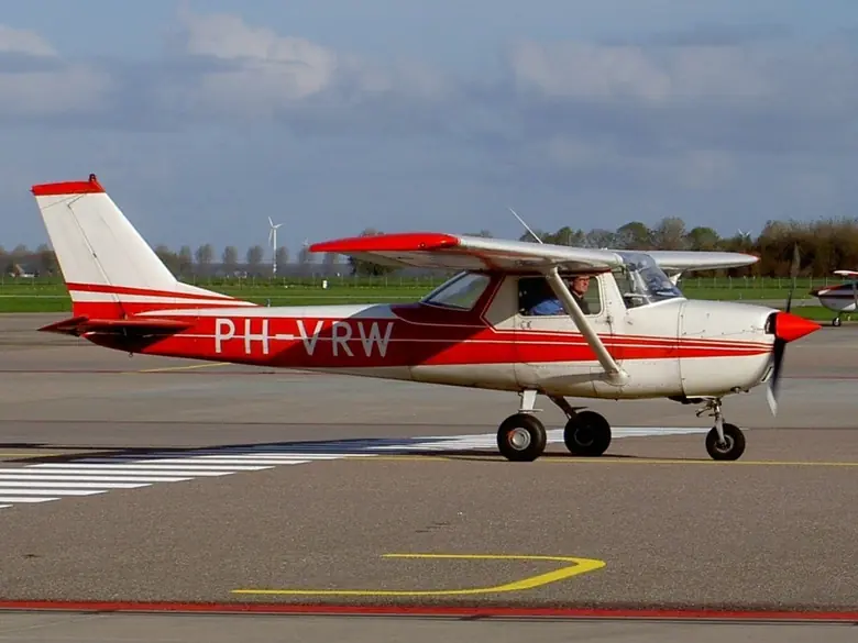 Red and white Cessna 150 taxiing on an airport apron with a runway marking behind it