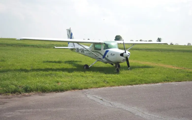 Cessna 152 parked on a paved strip beside a grass airfield under an overcast sky