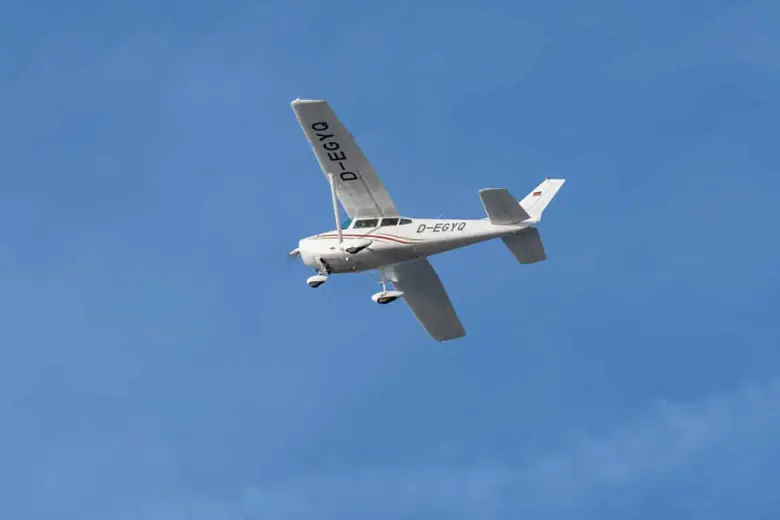White Cessna 182 Skylane banking over a blue sky seen from below