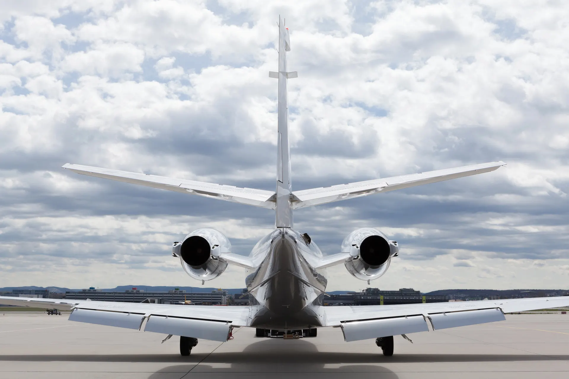 A white business jet seen from behind on an airport apron under heavy cloud