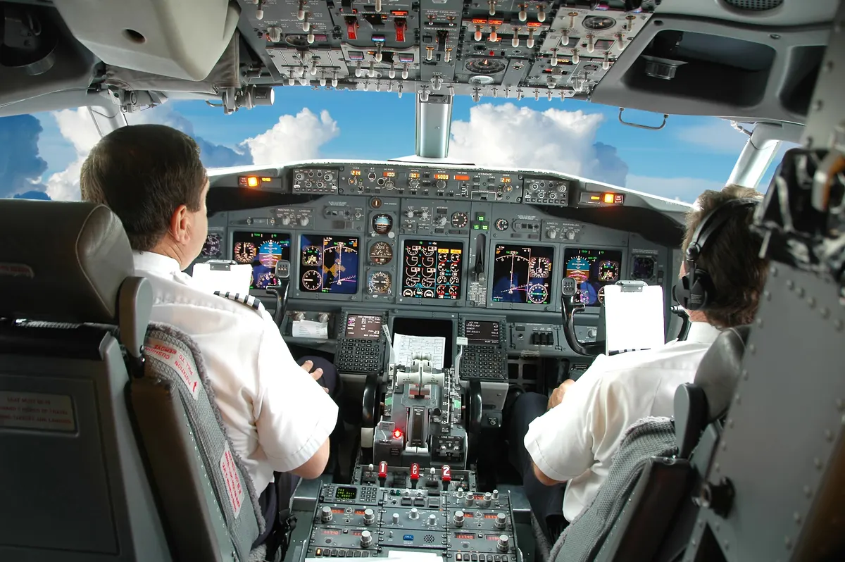 Two pilots seen from behind at the controls of an airliner cockpit