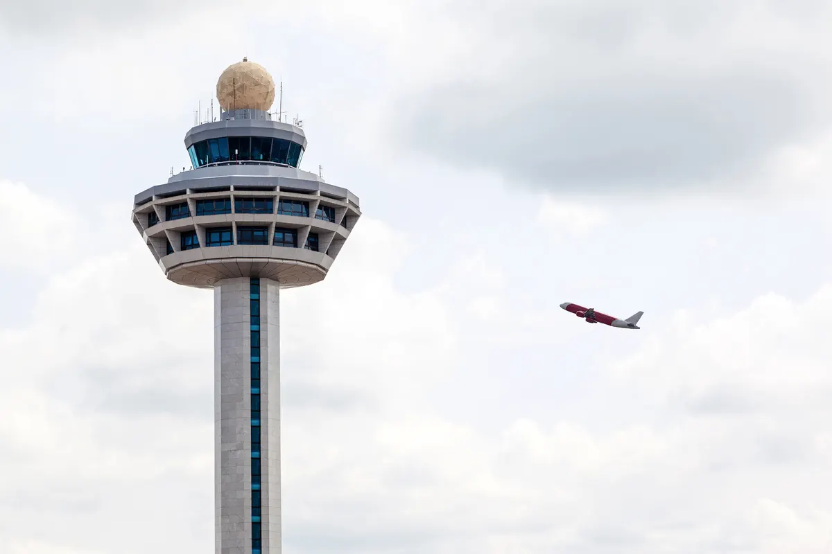 An airport control tower with a jet climbing away in the distance