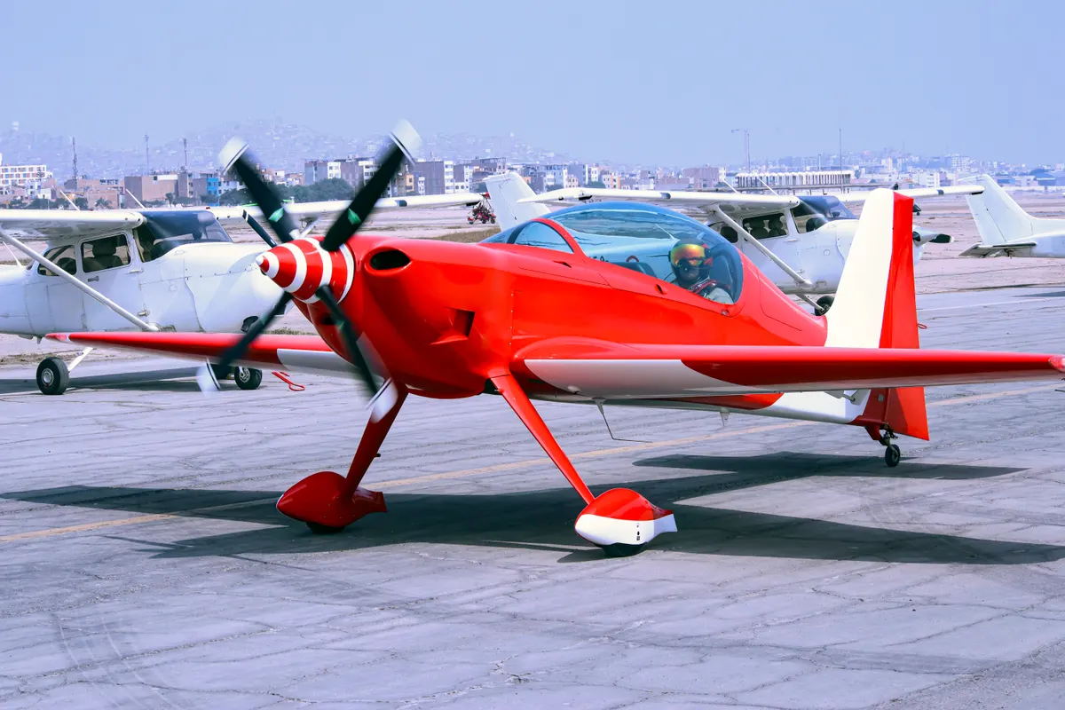 A red single-engine aerobatic airplane parked on an airport ramp