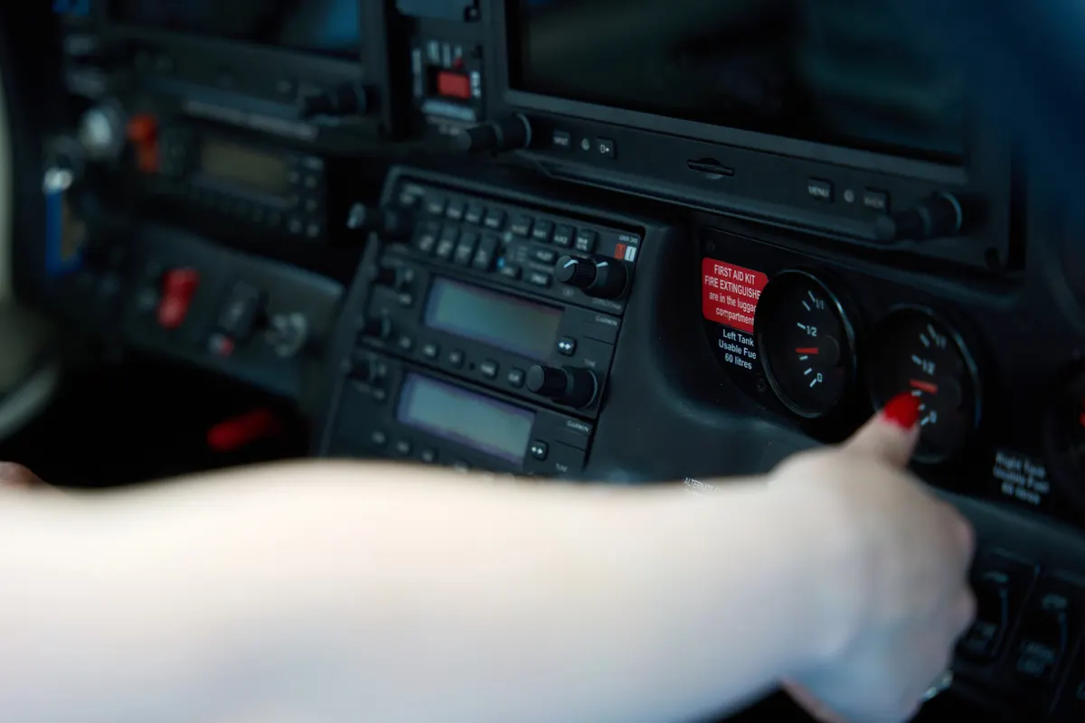 A student pilot's hand adjusting the avionics panel in a small airplane cockpit