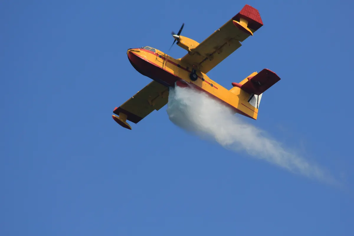 A yellow water-scooping amphibious aircraft releasing a load of water