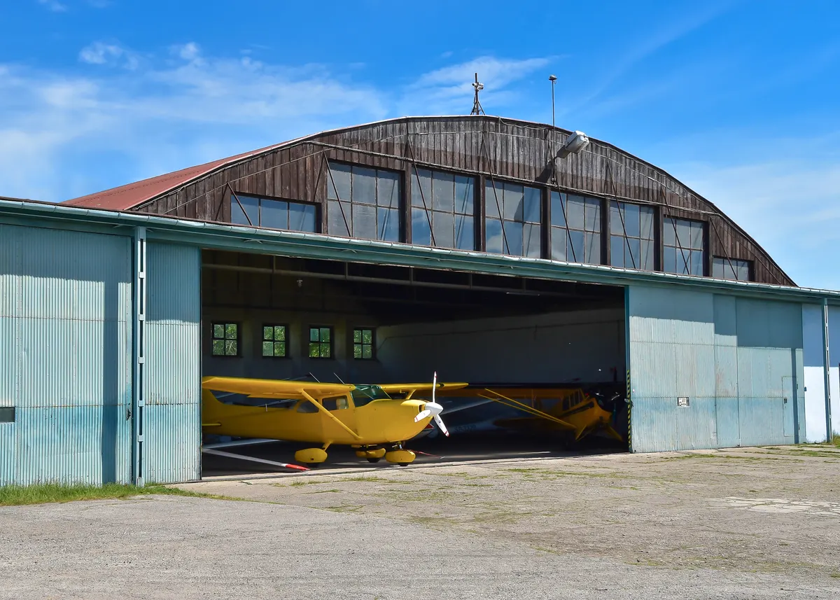 A yellow light airplane parked in an open hangar door on a sunny day