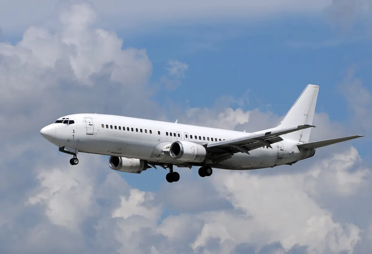A white passenger jet on approach under a cloudy sky