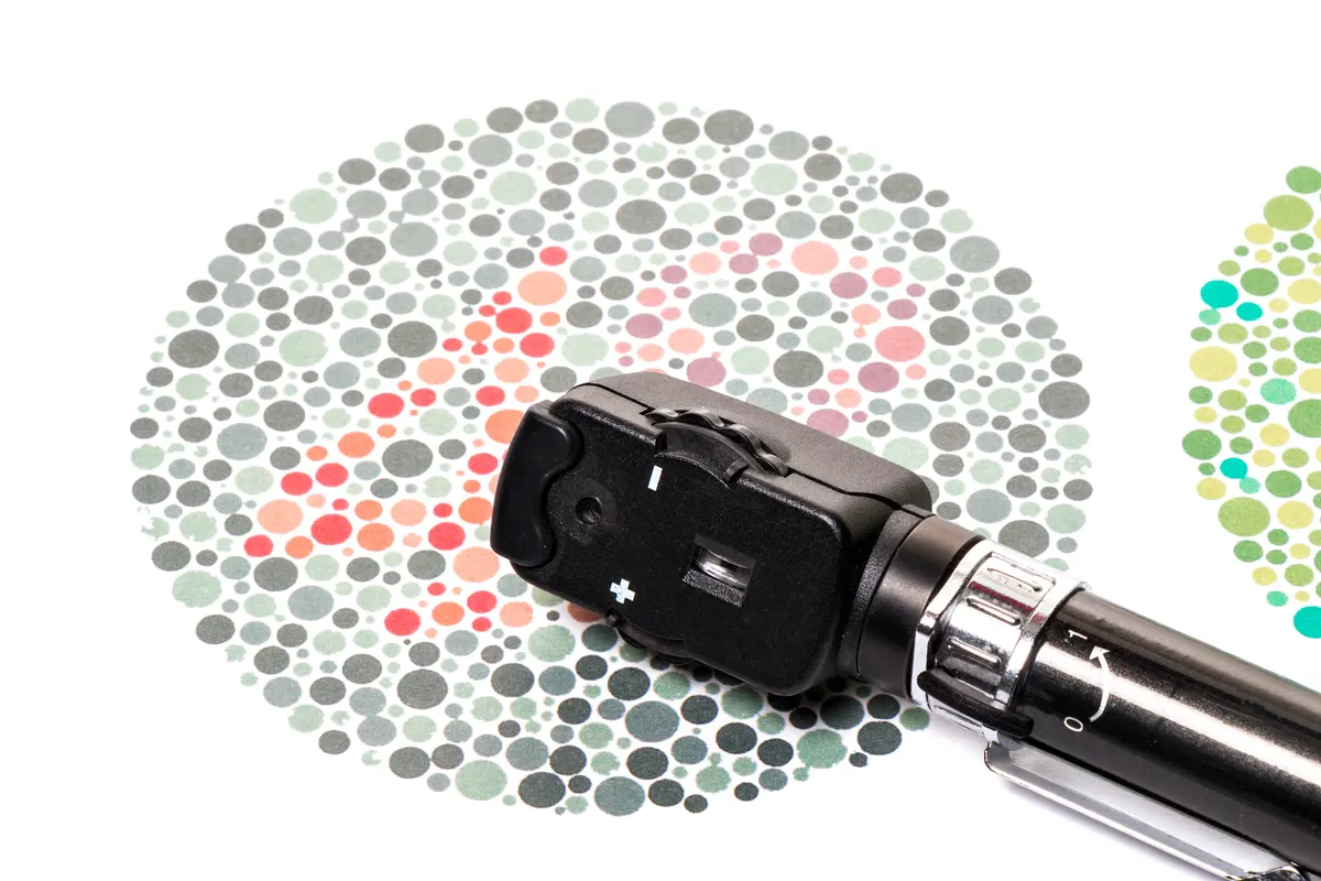 A color vision test plate with colored dots and an ophthalmoscope lying across it