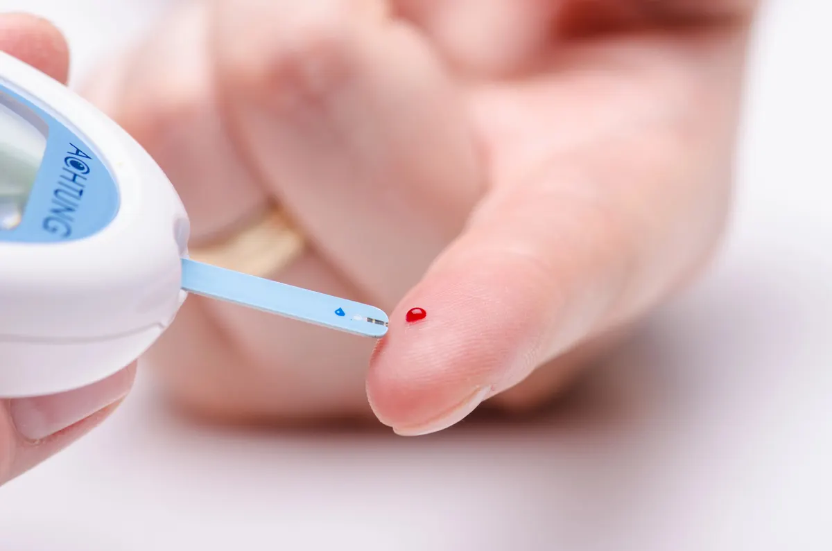 A blood glucose meter with a test strip touching a drop of blood on a fingertip