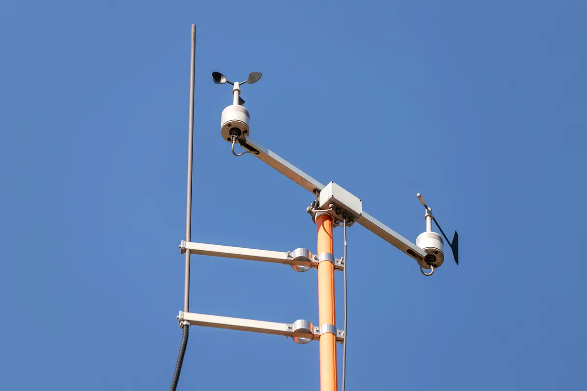A weather station mast with an anemometer and wind vane against a blue sky