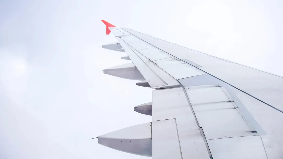 An airliner wing seen from the cabin window under a pale, cloudy sky